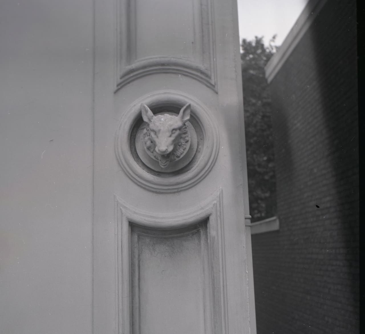 Zwart-witfoto uit 1958 van een gebeeldhouwde dierenkop in een rond medaillon op de gevel.
