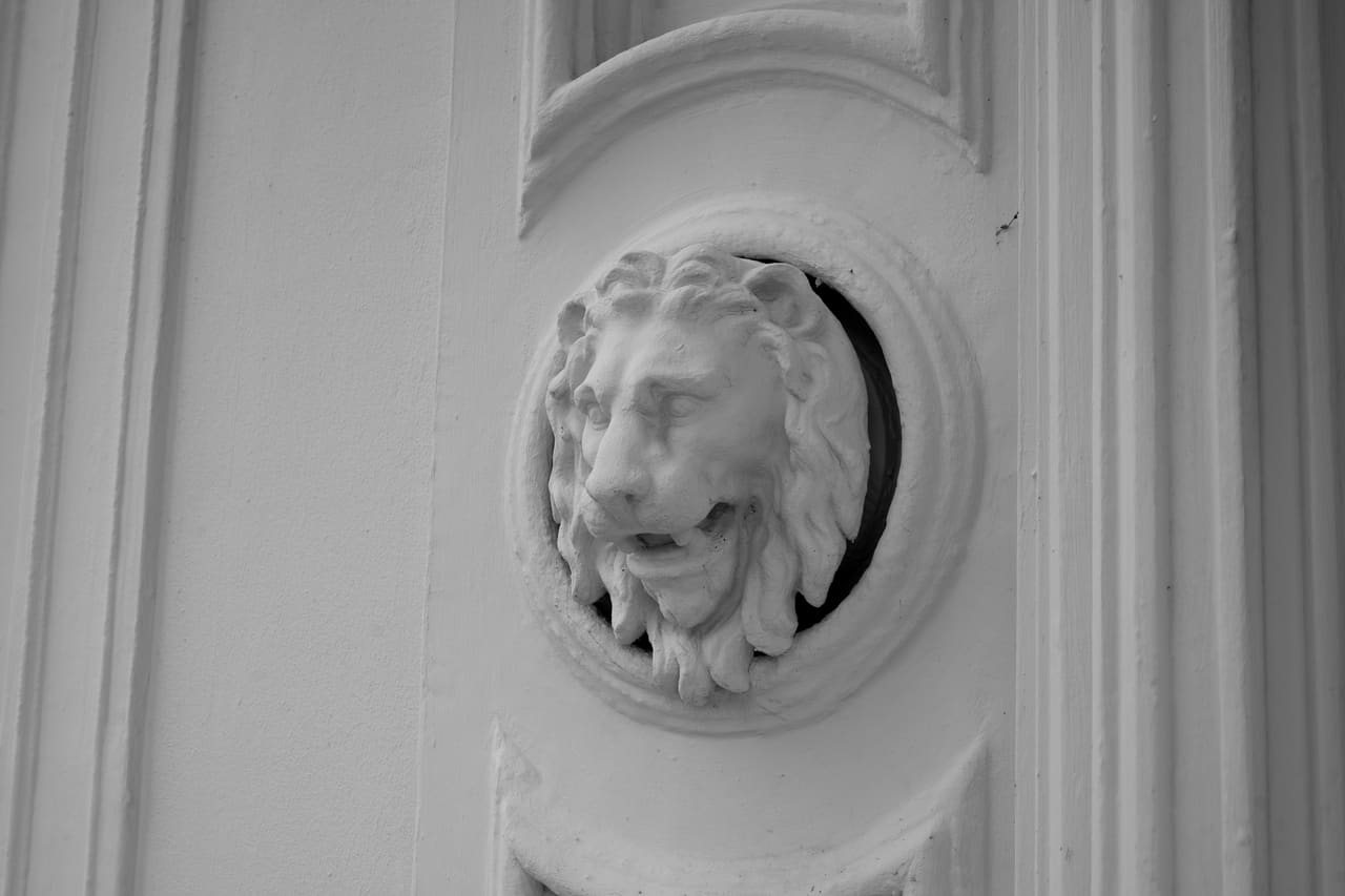 Detailopname van een gepleisterde leeuwekop in een rond medaillon op de gevel.