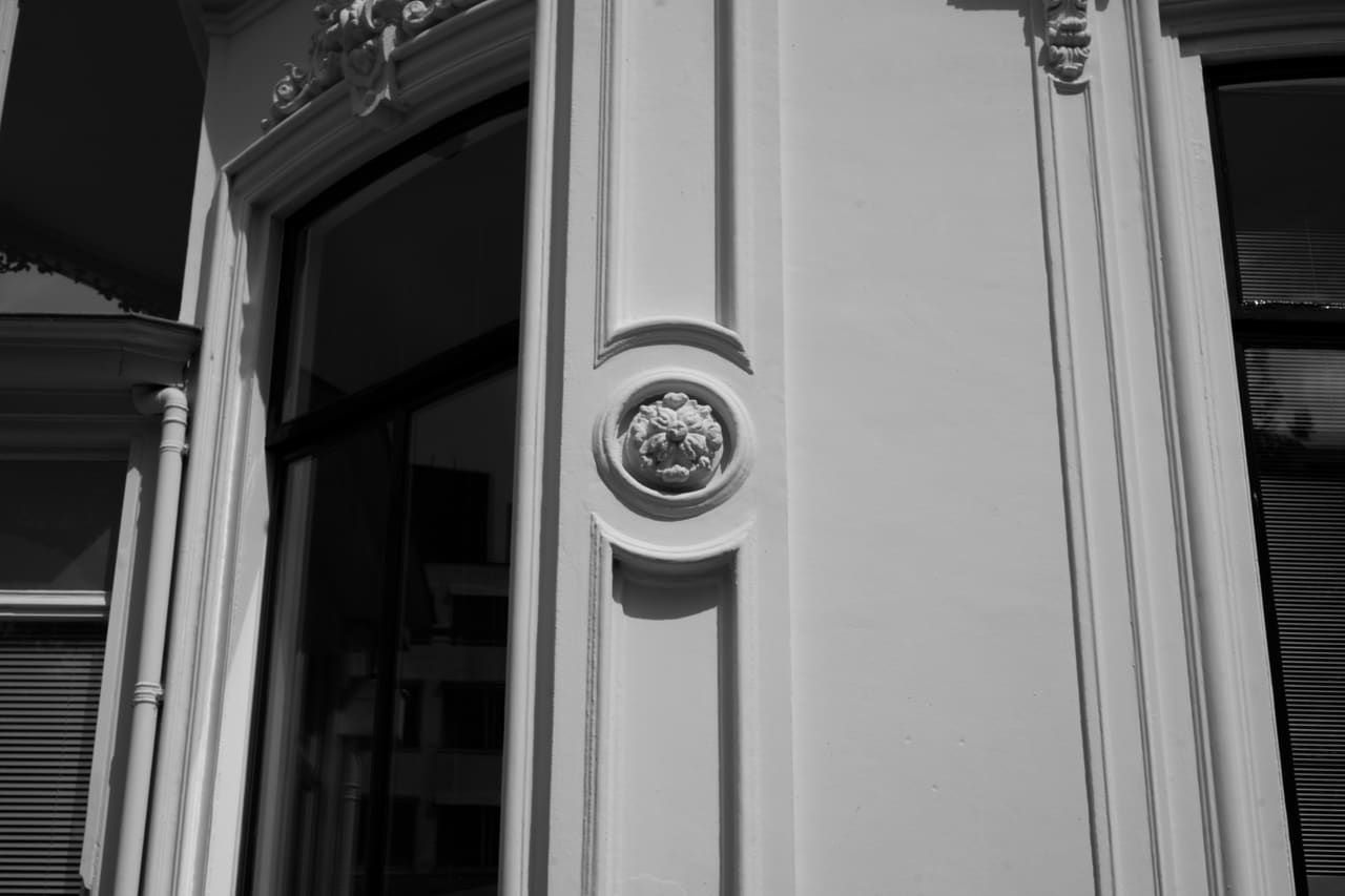 Detailopname van een rond rozet in het pleisterwerk naast een vensteromlijsting.