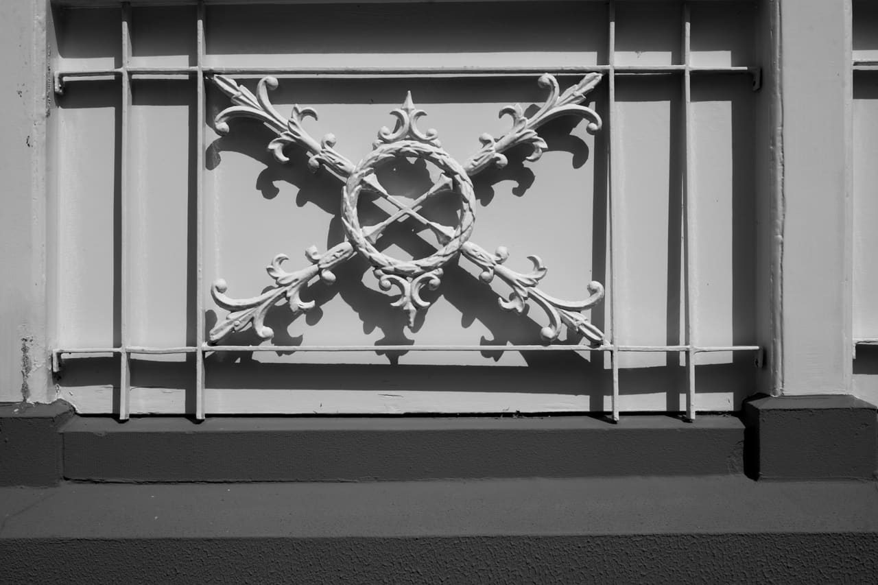 Zwart-witopname van een gietijzeren hek met gekruist siermotief voor de villa.