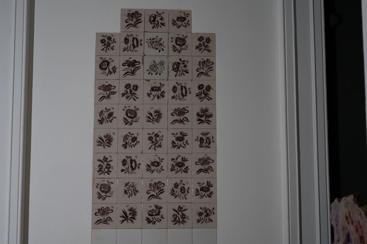 Tegeltableau met bloemmotieven op een witte wand in de kelder.
