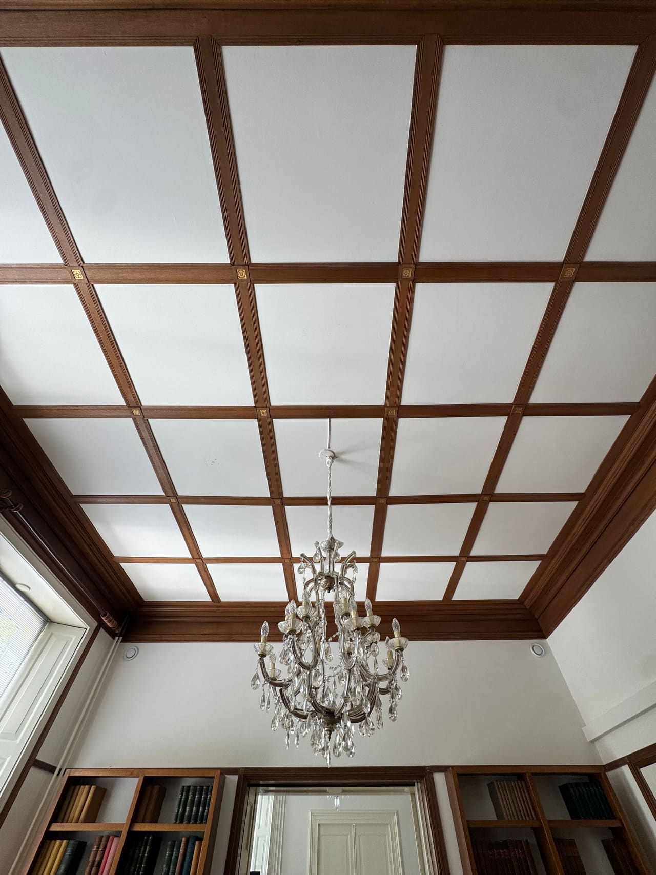 Houten cassetten-zoldering met een kroonluchter, van onderaf gefotografeerd.