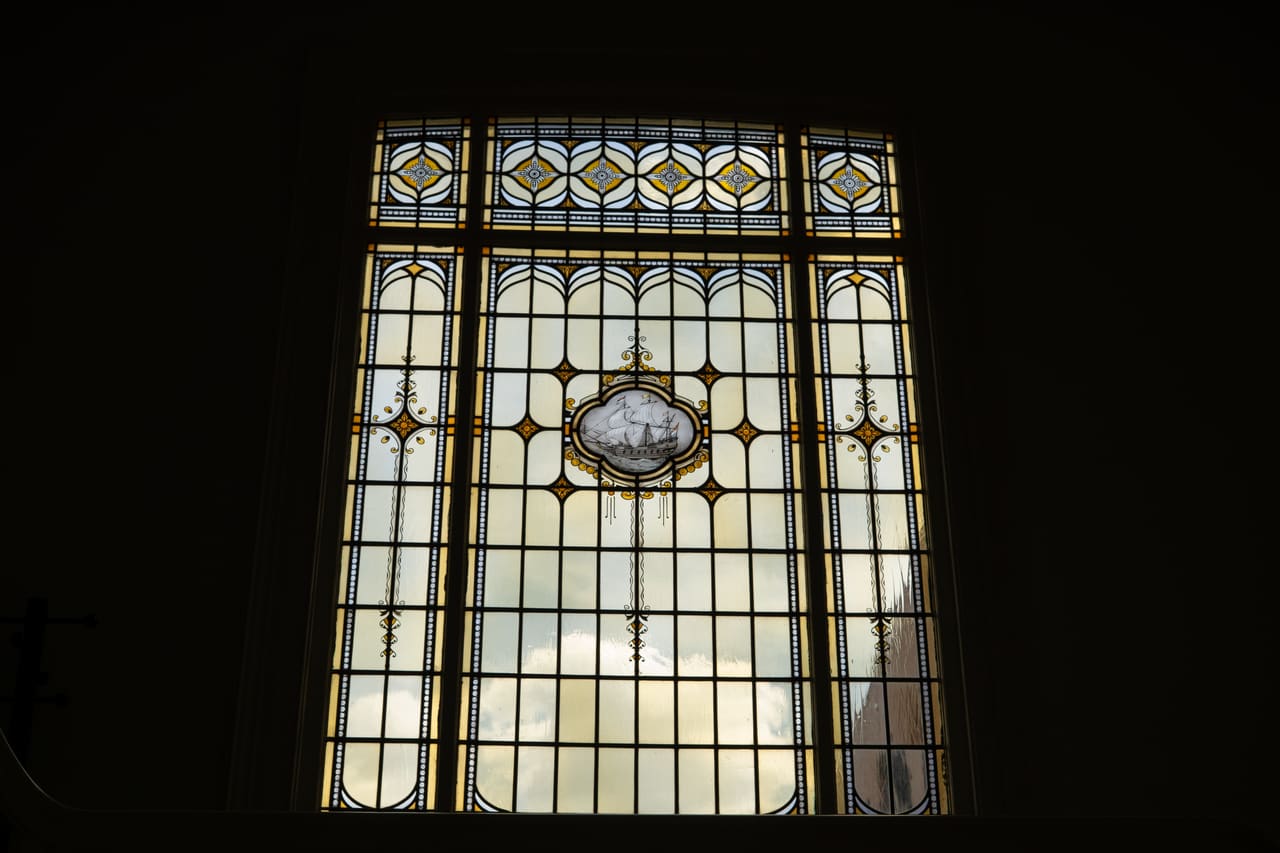 Hoog glas-in-loodvenster in tegenlicht, met een geschilderd medaillon in het midden.