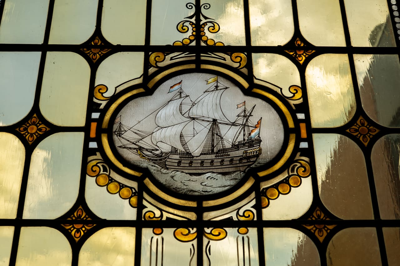 Gebrandschilderd medaillon met een driemaster in een glas-in-loodvenster.