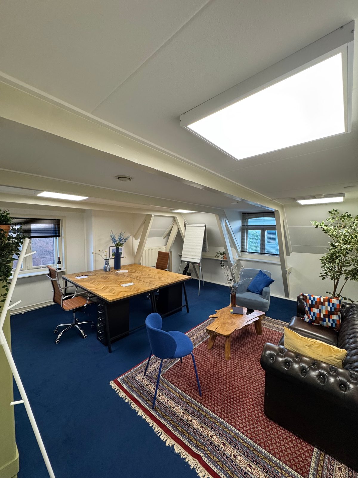 Kantoorkamer met werktafel, zithoek en dakramen.