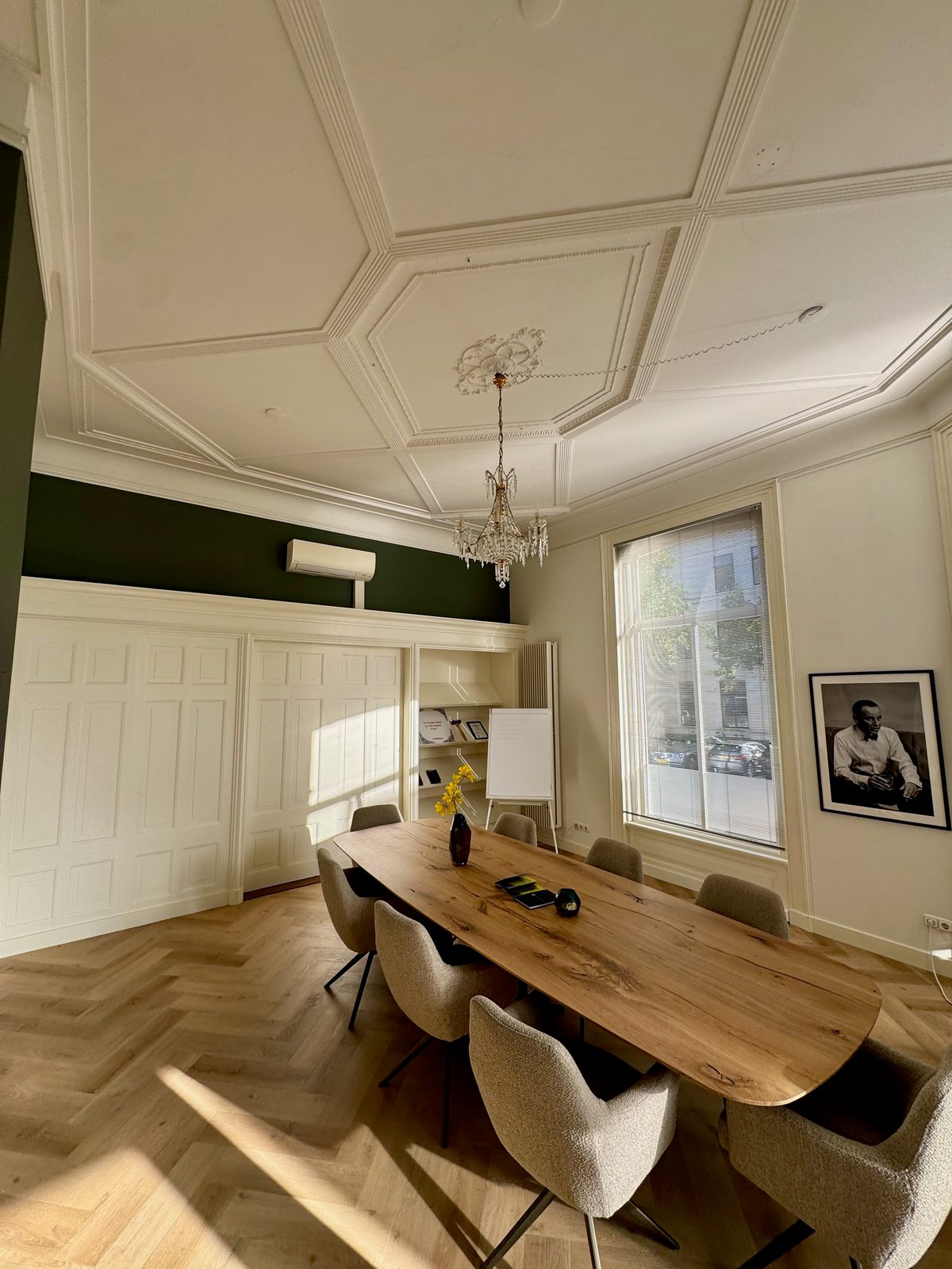 Vergadertafel met stoelen naast de groene wand en witte kasten.